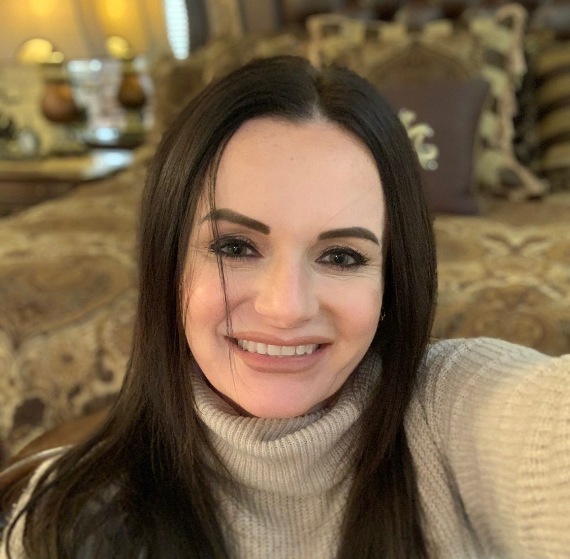 A smiling woman with long dark hair wearing a beige turtleneck sweater.