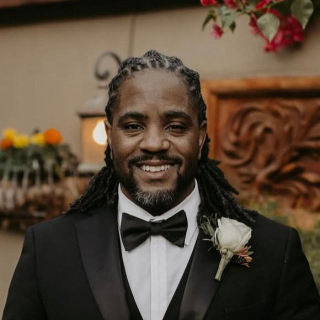 Smiling groom in tuxedo with boutonniere at BU Resource Center, showcasing professional event setup.