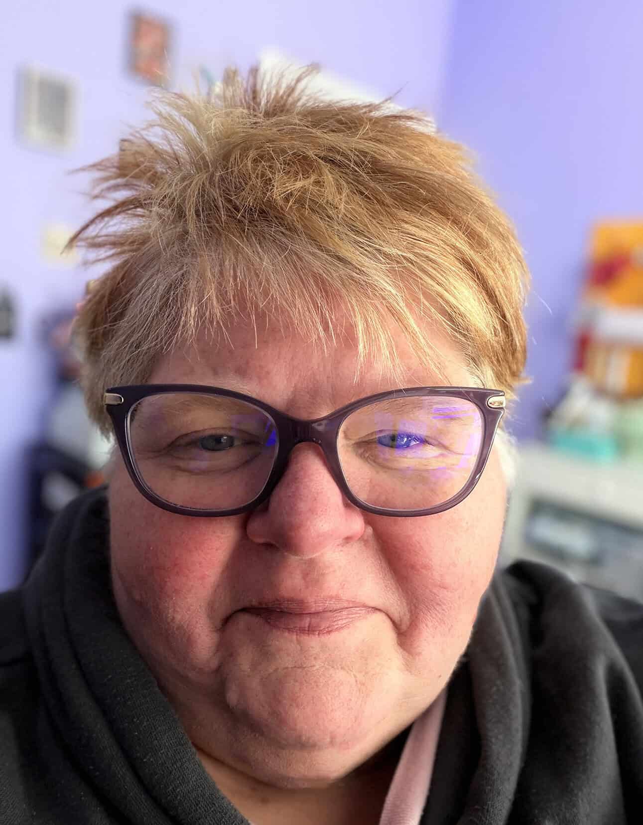 Close-up selfie of a person with short blonde hair and dark-rimmed glasses.