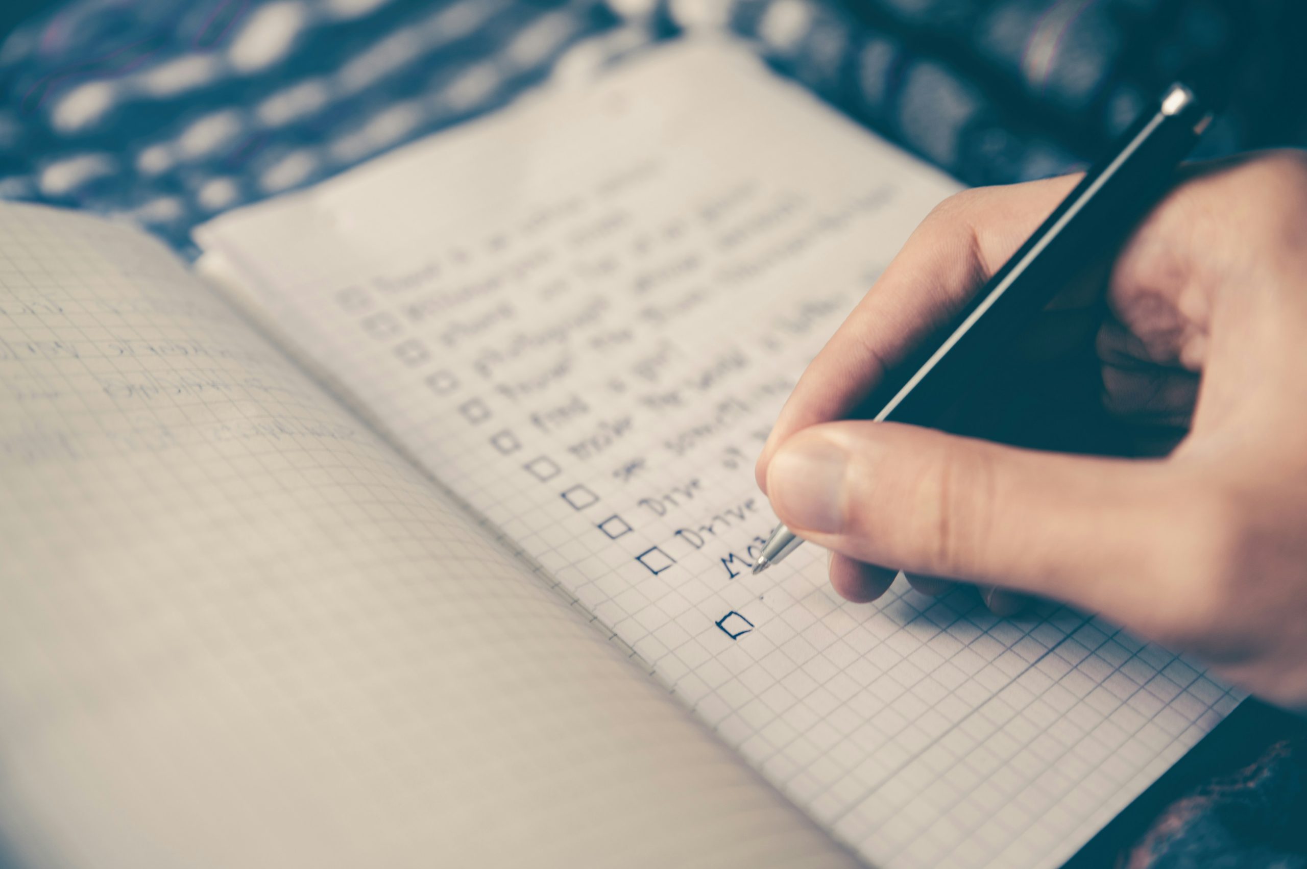 Hand holding a pen writing on a checklist in a notebook.