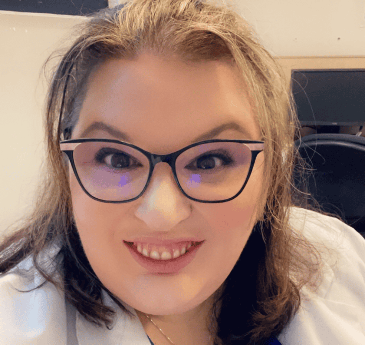 A smiling woman with blonde hair wearing black glasses and a white shirt.
